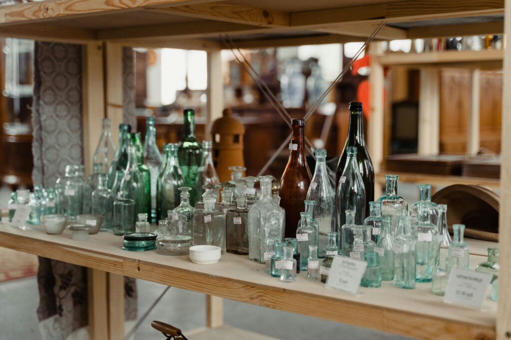 Assorted vintage glass bottles showcased on wooden shelves in an antique store setting.